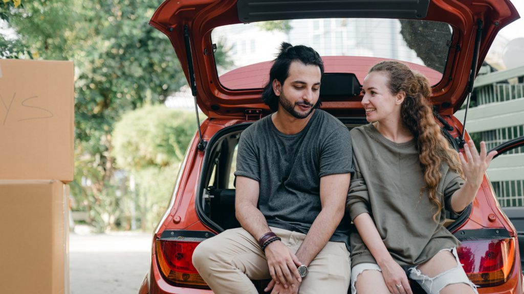 Young diverse couple relaxing after unpacking car while moving home